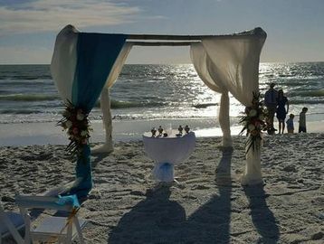 Beach wedding setup with a decorated arch and table at sunset.
