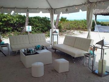 Outdoor seating area with white sofas and lanterns under a canopy on sandy ground.