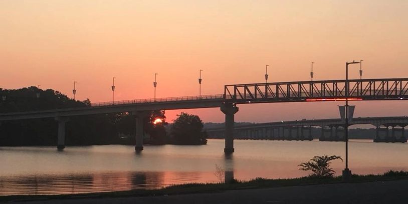 Sunset over a calm river with bridges silhouetted against the sky.