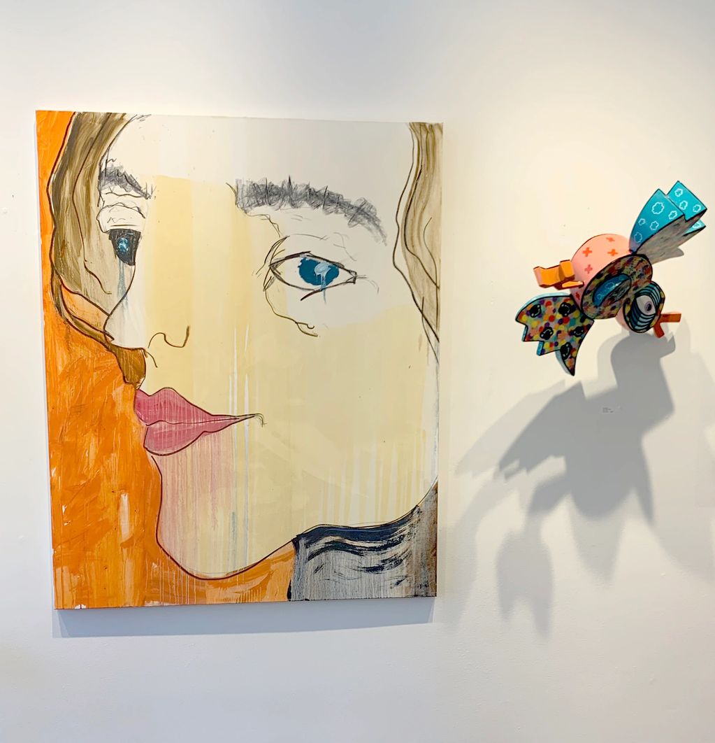 Abstract portrait painting with a colorful bird sculpture casting a shadow on the wall.