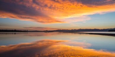 Sunset over a calm lake reflecting orange clouds.