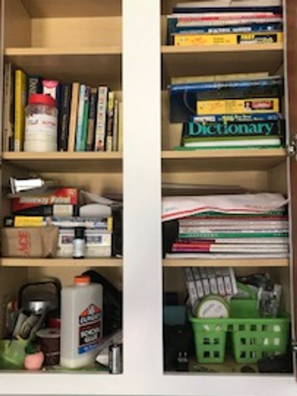 Books and other stuff in an unorganized cabinet.