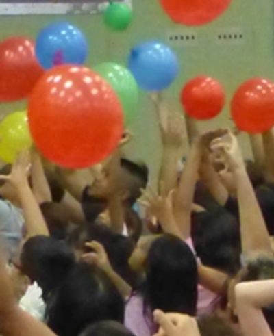 Children playing with colorful balloons in a crowded indoor space.