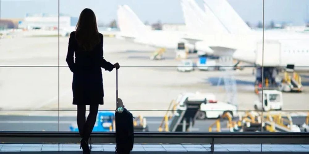 Flight Attendant, airline crew, in airport, looking out terminal window. Airplanes at airport gate.