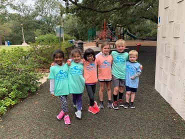 Six children standing together at a playground, smiling and wearing colorful shirts.