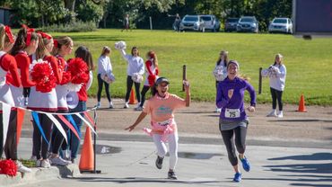 Two girls race in a relay event while cheerleaders and spectators watch.