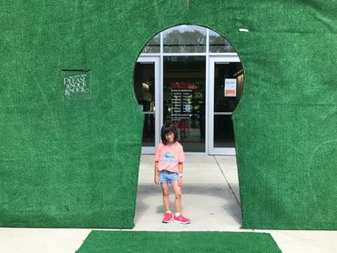 A young girl stands in a giant keyhole-shaped green structure at an entrance.