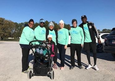 Group wearing matching teal shirts posing outdoors with a stroller under clear blue sky.