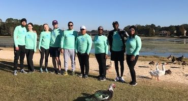 Group of people in matching teal shirts posing near a lakeside with birds.