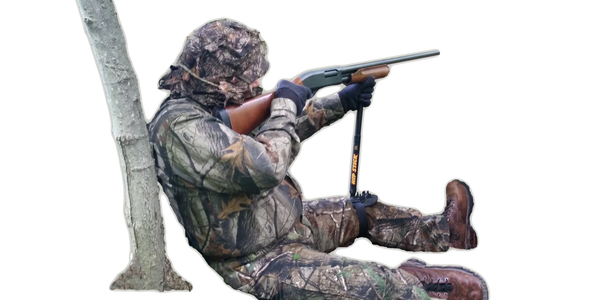 Turkey hunter on the ground using a shooting stick on his knee to steady his firearm
