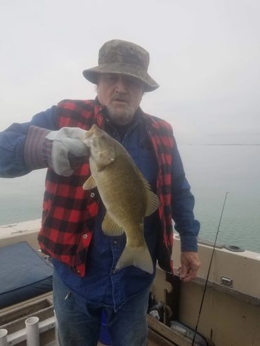 Man holding a freshly caught fish on a boat in foggy weather.