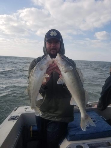 Man on boat holding two large fish he caught.