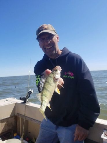 Man proudly holding a freshly caught fish on a boat under clear blue skies.