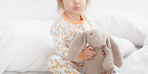 toddler girl sitting on bed with a stuffed animal bunny in her lap, toddler sleep help, illinois sle