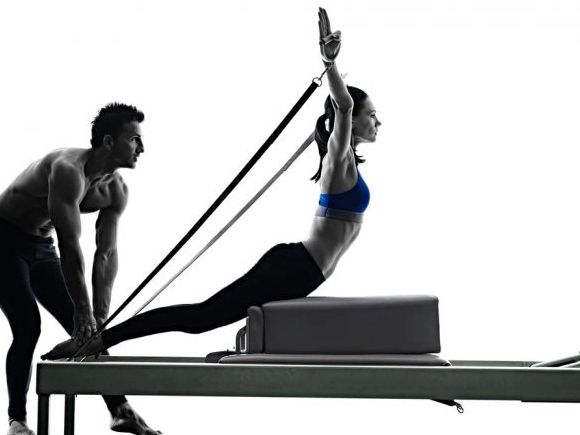 Reformer pilates near me guy is helping lady to exercise 