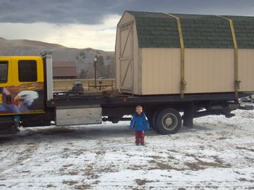 large shed tied down on flatbed of large yellow tow truck