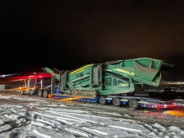 tow truck tows large piece of heavy machinery down a snowy road at night
