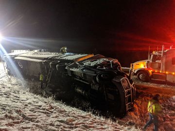 large semi truck over turned on the side of the highway at night in the snow