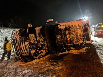 over turned semi covered in snow on the side of the road at night
