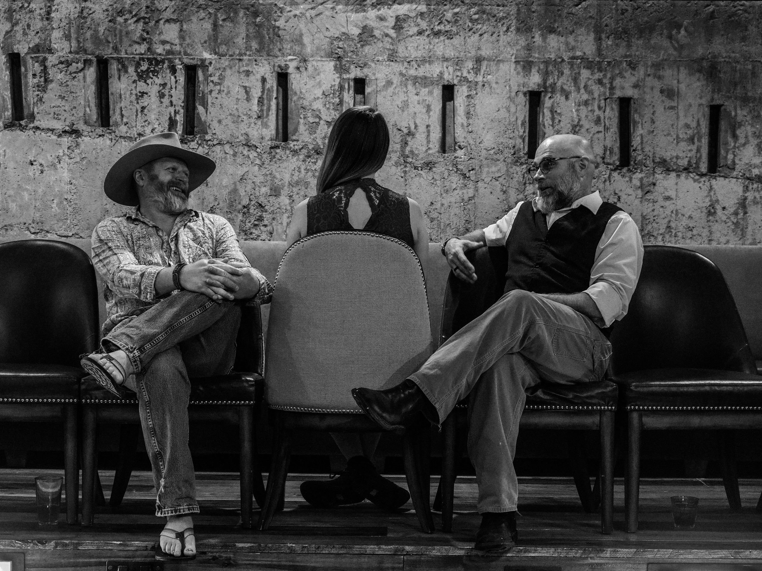 Three people sitting on chairs facing each other in a rustic setting.