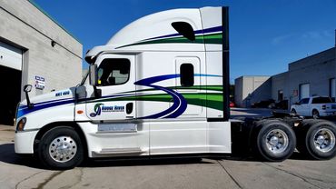 White semi-truck with blue and green stripes parked near industrial buildings.